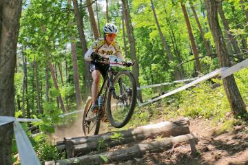 山の中の険しいコースに横たわる木の上をマウンテンバイクで飛び越えている選手の写真
