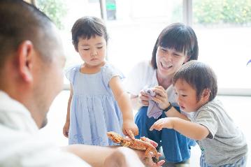 男性の手にのっているトカゲを子供たちが指で触り、お母さんが見守っている写真