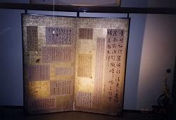 金の屏風にいくつもの漢字で書かれた白い紙が貼られている二枚折屏風片双の写真