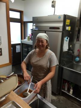 厨房で笑顔で料理をしている中村さん（奥様）の写真