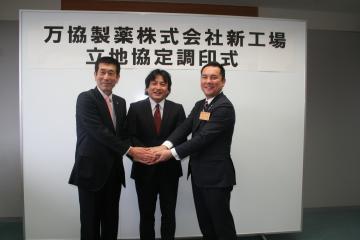 調印式で町長と万協製薬株式会社の代表の方2名と手を握り記念撮影をしている写真