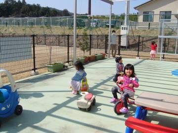 テラスで三輪車やおもちゃの車に乗って遊んでいる子供たちの写真