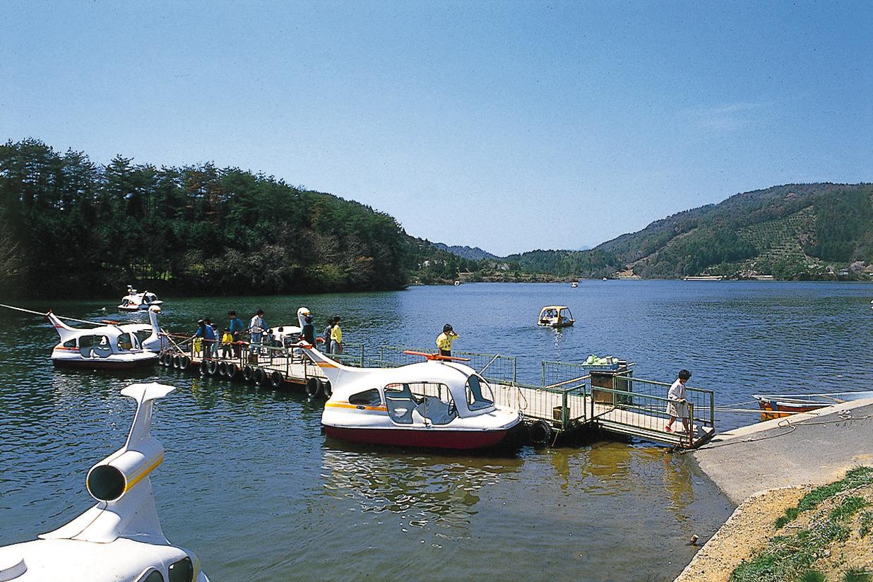 山の中にある大きな池の白鳥のボート乗り場に何人かの人が集まっている写真