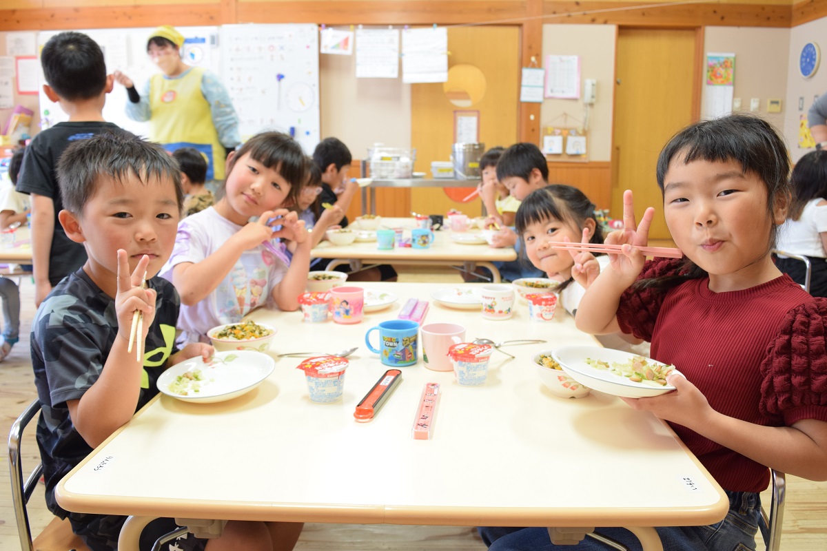 園児たちが机に座り給食前にいただきますの手を合わせている写真