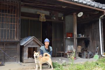 古い民家の玄関前に柴犬と移住者の方がいる写真